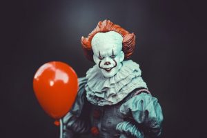 Scary clown holding red balloon