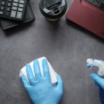 Spring cleaning technology- gloved hands wiping down a desk with a red laptop, calculator and coffee cup on top of desk