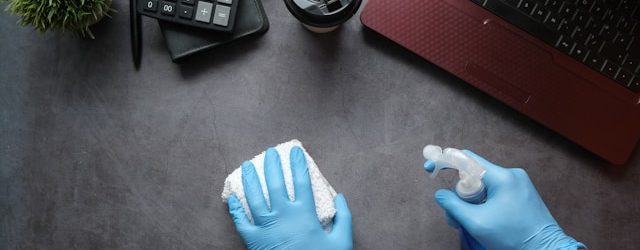 Spring cleaning technology- gloved hands wiping down a desk with a red laptop, calculator and coffee cup on top of desk